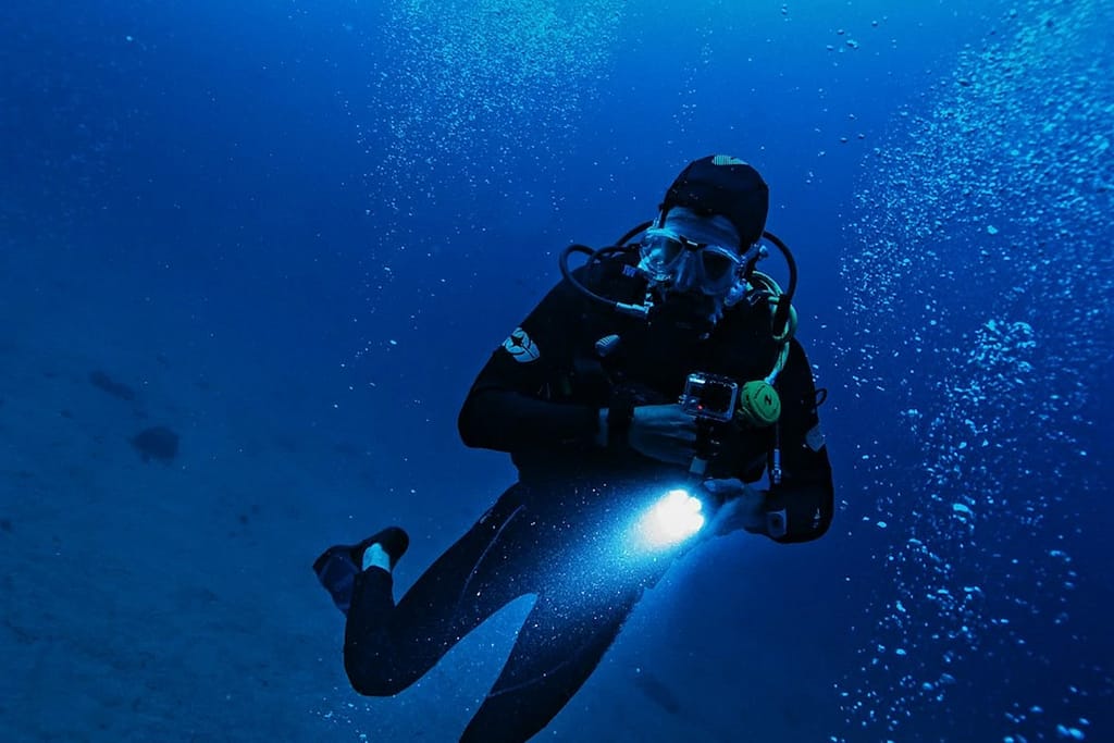 A diver with a light underwater in a night dive, alone in the dark and a lot of bubbles around him. 