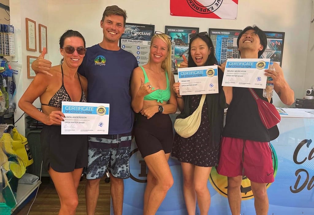 3 new open water divers happy holding they certificate on their hands and their two diving instructors