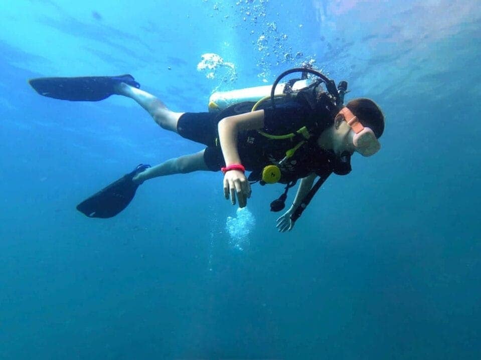 A diver in full gear underwater and a sun light coming through the sea